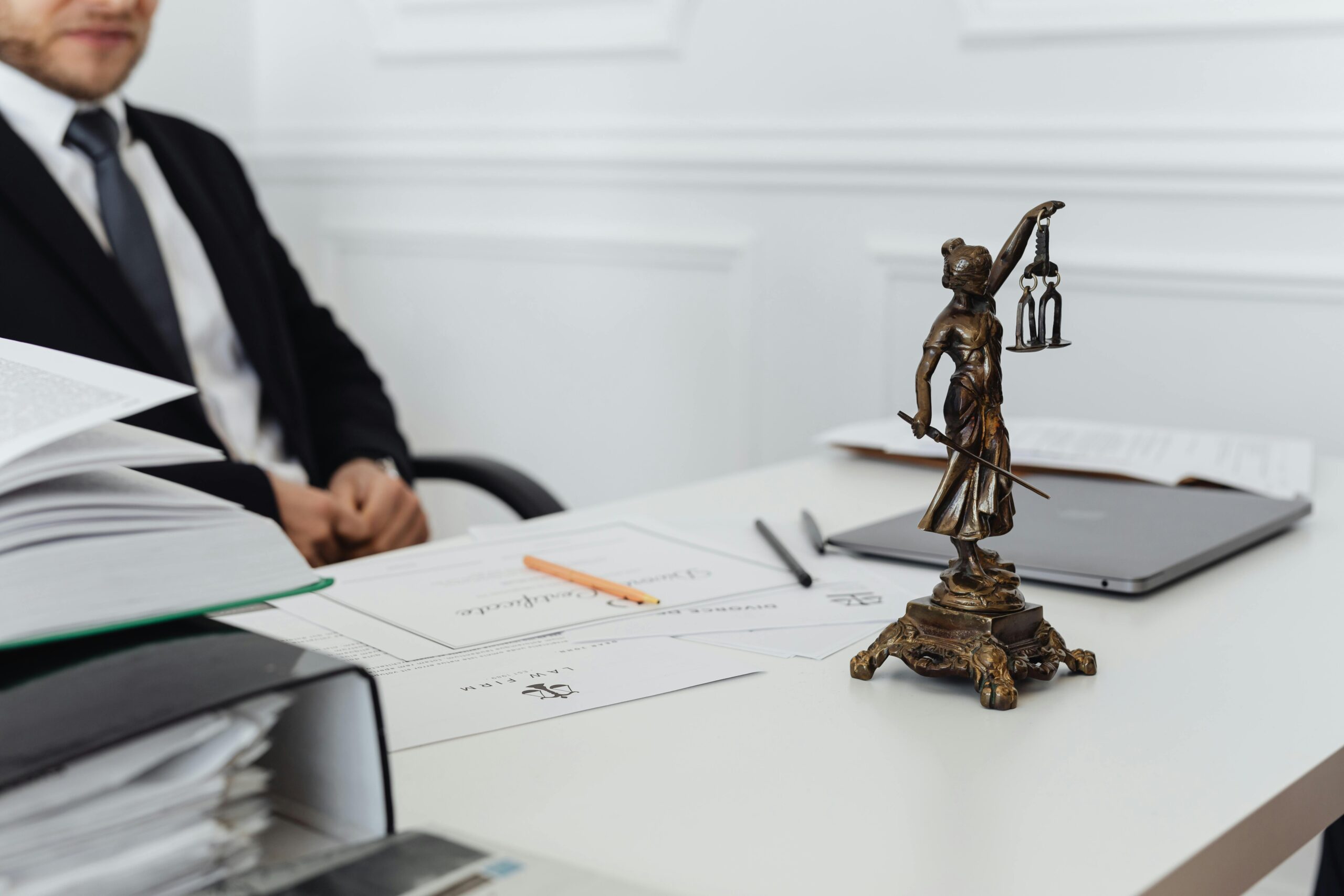 A man in front of legal papers and a statue of Lady Justice